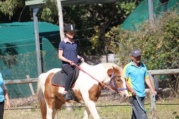 Person riding a pony with a handler in an outdoor setting. The pony is brown and white.
