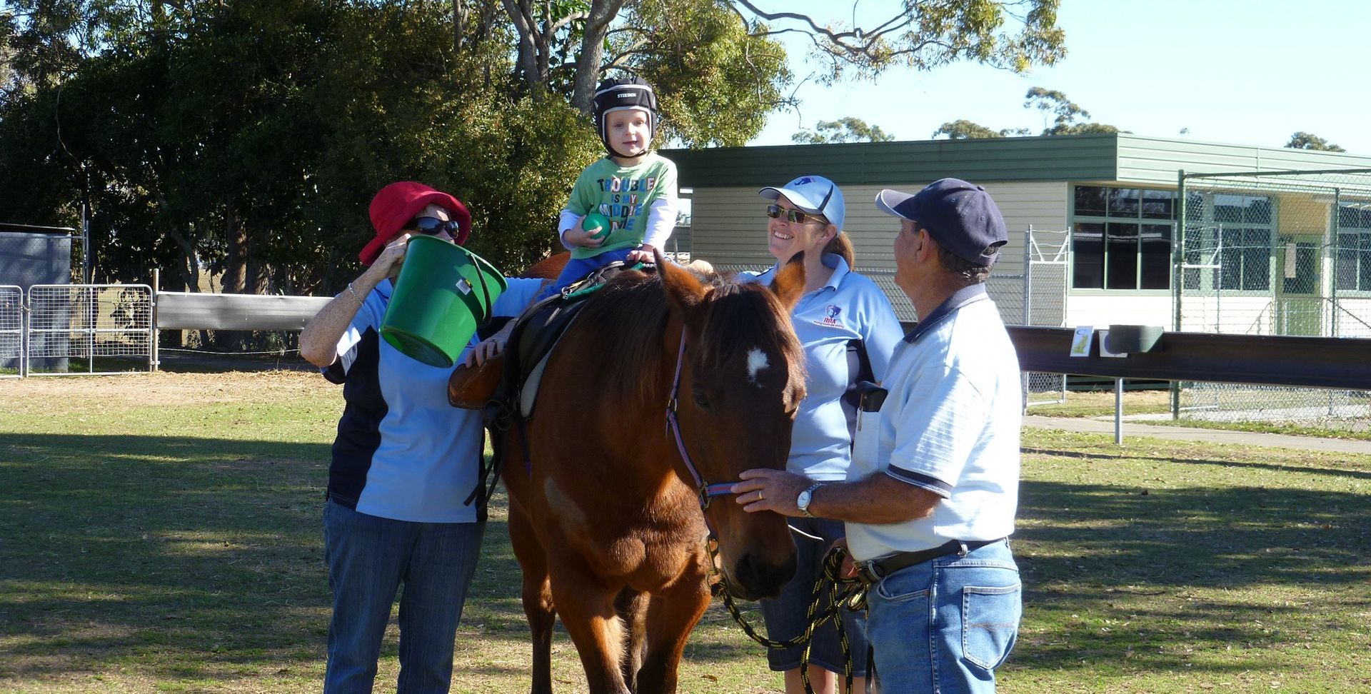 Child on a horse, being splashed with water by two people with a fourth person holding the reins, outdoor setting.