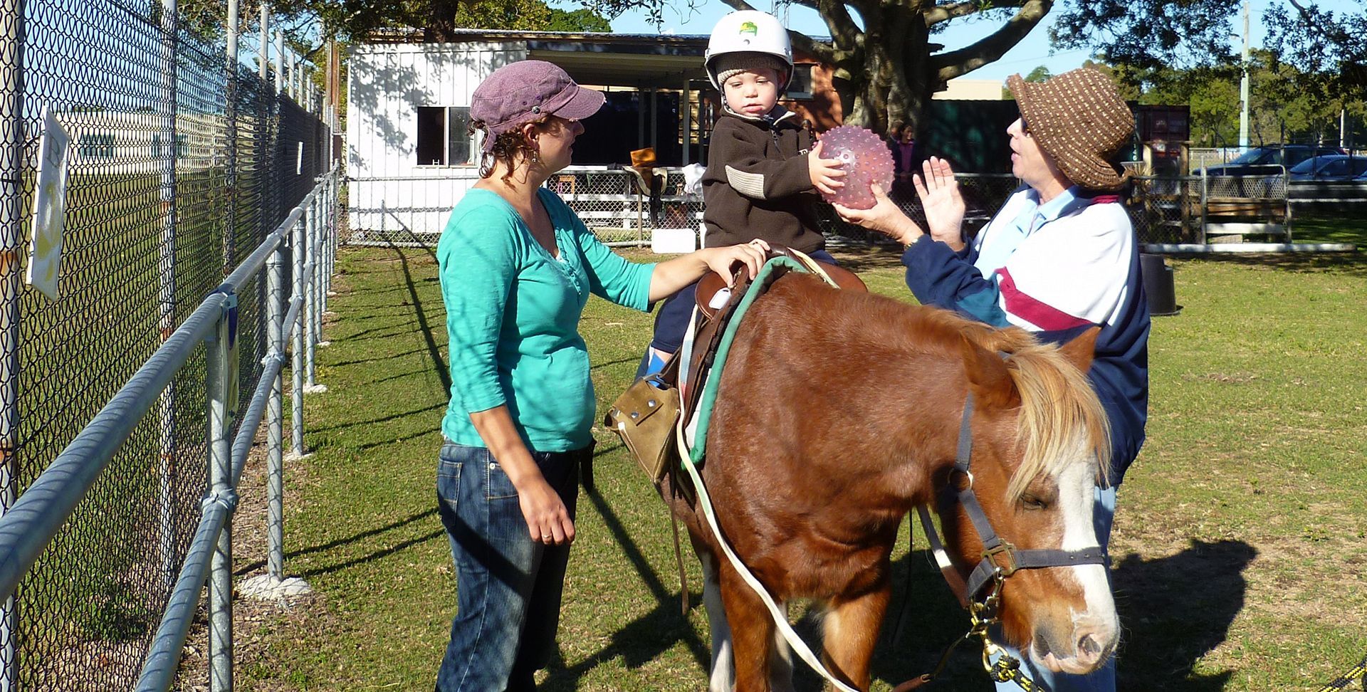 Woman helps a child ride a pony at an outdoor event, other woman nearby.
