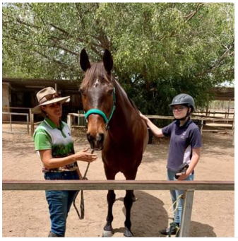 Woman and girl with a brown horse. They are petting the horse in an outdoor setting.