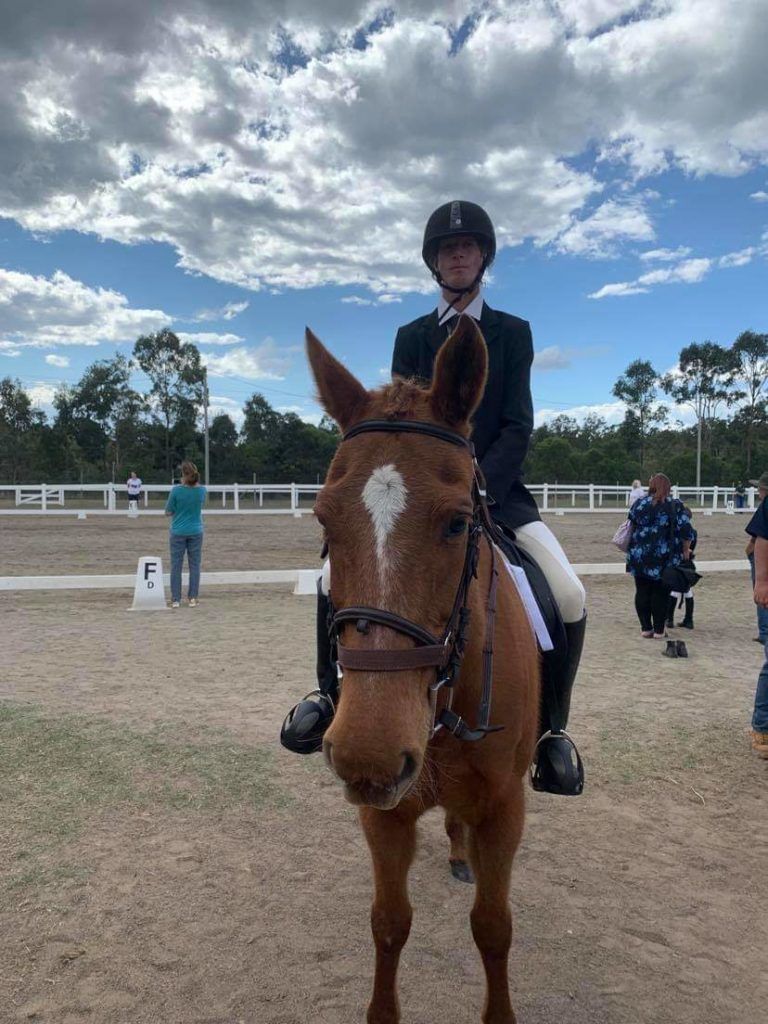 A rider on a brown horse in a dressage arena, wearing formal attire. Cloudy sky.