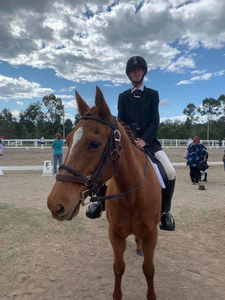 A rider on a chestnut horse at an equestrian event, both looking toward the camera; outdoor setting.