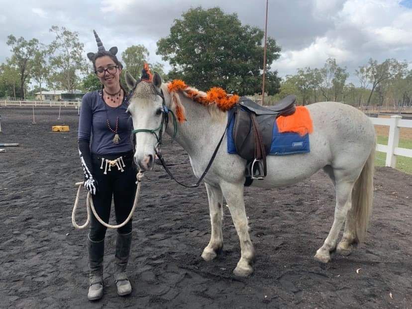 Woman in costume with a unicorn-adorned horse in an outdoor riding arena.