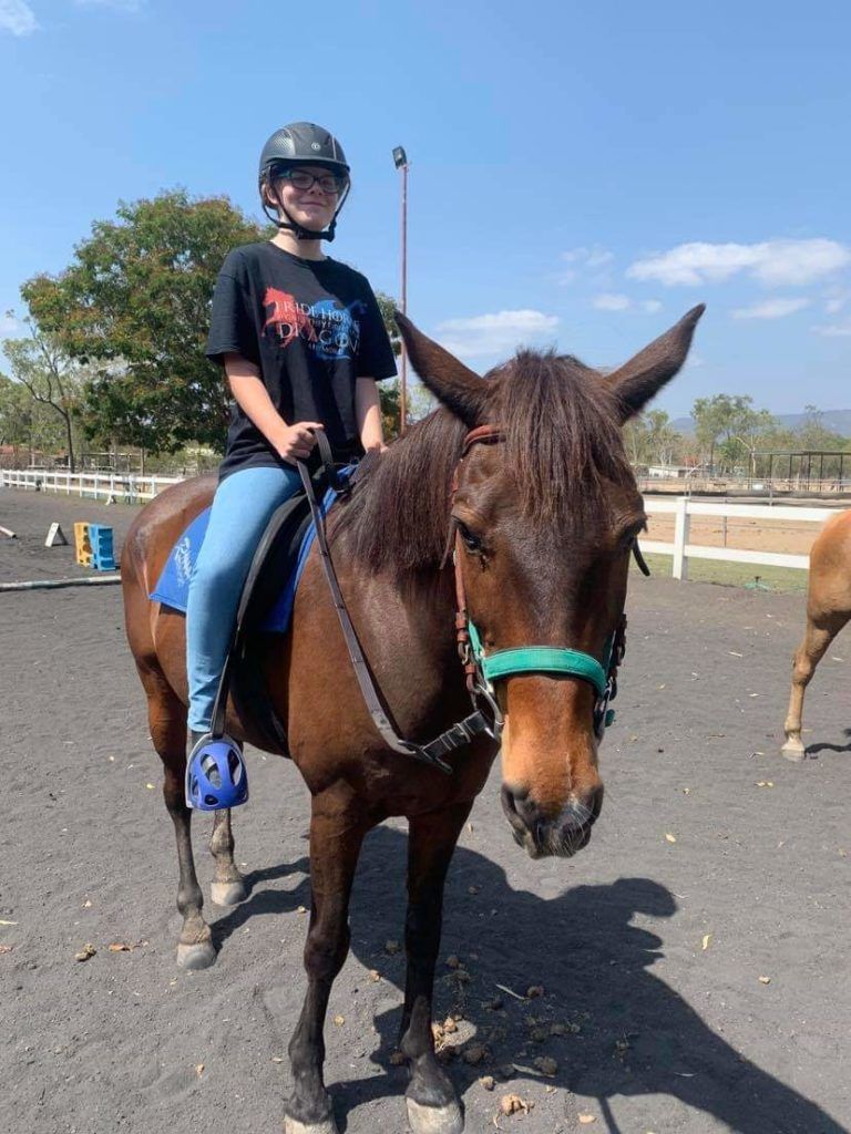Person wearing a helmet riding a brown mule in an outdoor arena.
