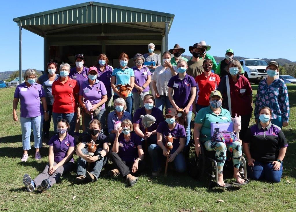 Group of people in purple shirts and masks pose outdoors. Shelter in the background.
