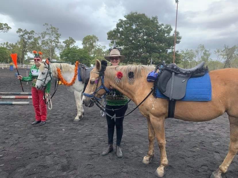 Two people with horses decorated for a holiday; outdoor arena setting. One person holds a pole.