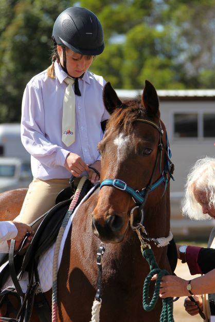 Young rider on a brown horse at an equestrian event, wearing a helmet and formal attire.