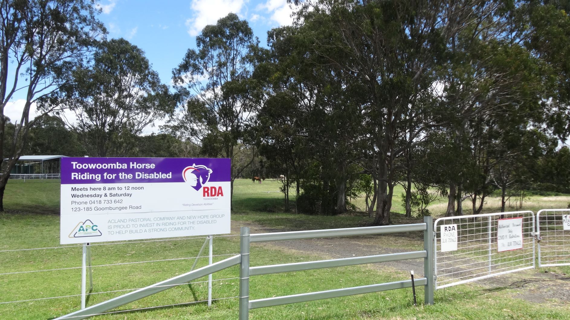 Sign for Toowoomba Home Riding for the Disabled with trees and a fence in the background.