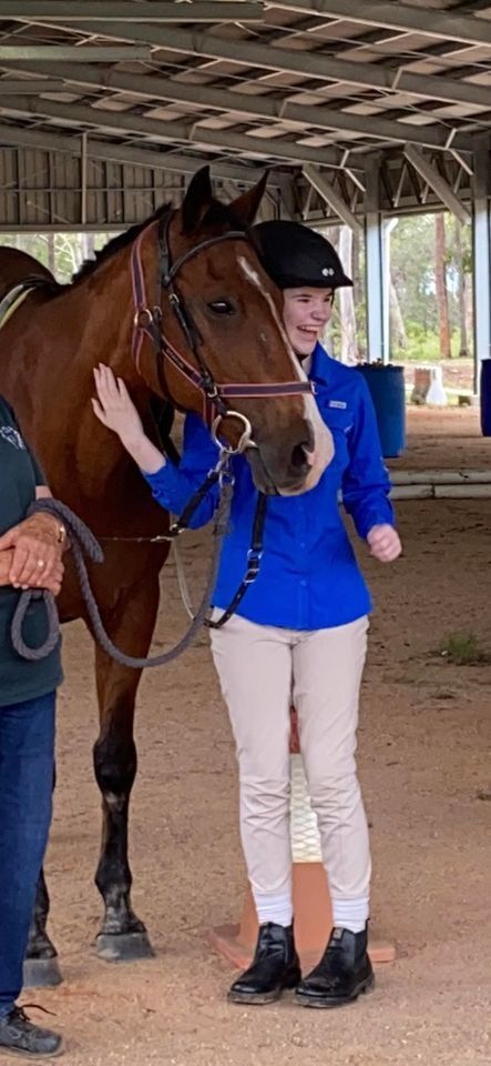 A woman in a blue jacket pets a brown horse in an indoor arena.