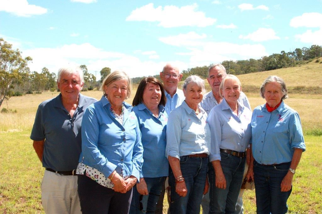 Group of people in blue shirts stand in a field with trees in the background.