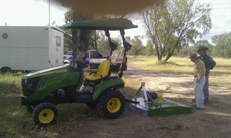 Green John Deere tractor with two people in a field, under a canopy.