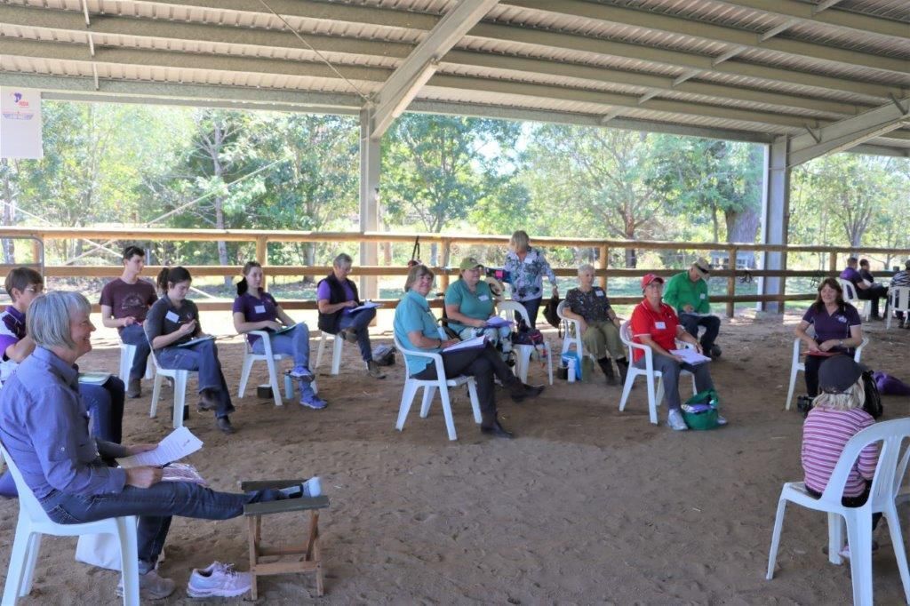 People sitting in chairs under a covered arena, attending a meeting.
