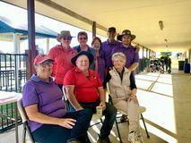 Group of people in purple and red shirts, under a covered area, smiling.