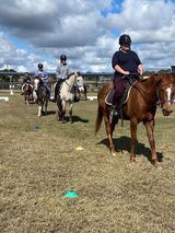 People riding horses in an outdoor equestrian training area with cones on the ground.