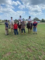 People with horses in a grassy field on a cloudy day. Several riders and ground crew pose.