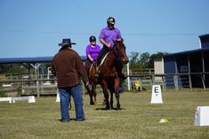 Horseback riding lesson; instructor watches riders on horses in outdoor arena.