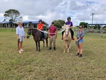 People on horses with helpers in an outdoor riding arena.