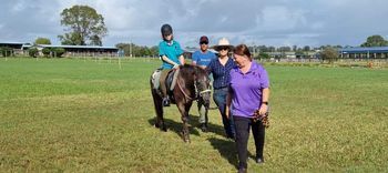 A person rides a pony, guided by several people, on a grassy field.