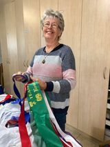 Woman smiling, holding colorful ribbons. In front of a light-colored wardrobe.