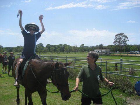 Person on horseback raises arms, celebrating, as another person leads the horse outdoors near a fence.