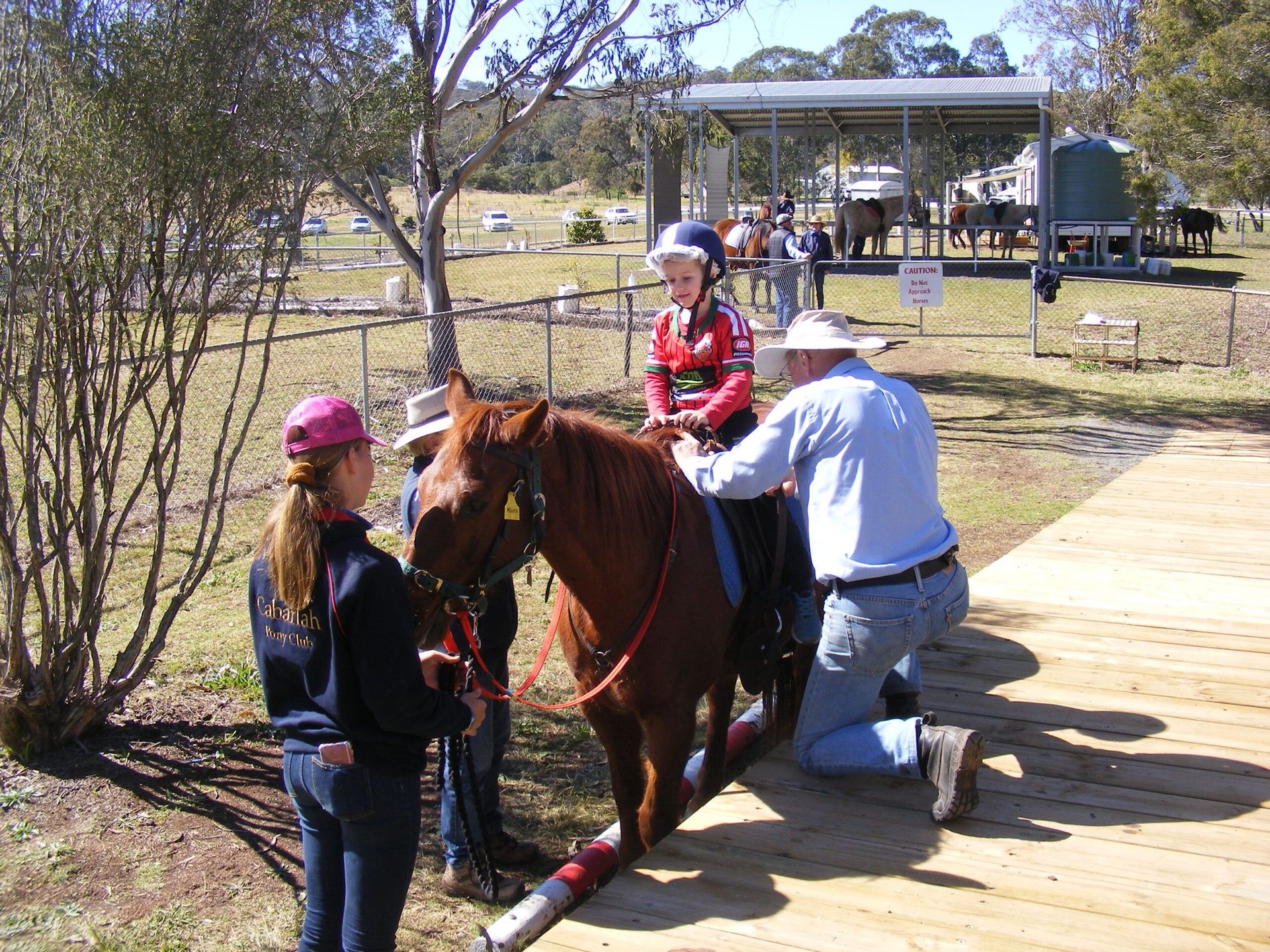A person riding a horse with assistance from two people, in an outdoor setting.