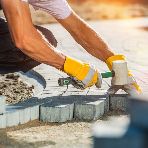 a man wearing yellow gloves is kneeling down while holding a hammer .