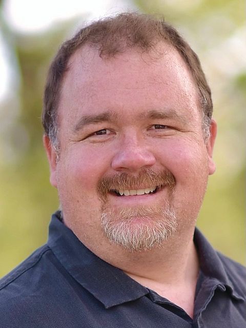 A woman wearing glasses and a white shirt is smiling for the camera.