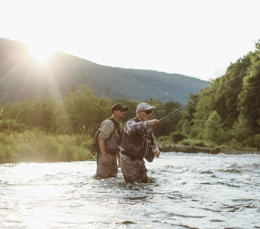 Photo of men waist-deep in a stream doing fly-fishing.