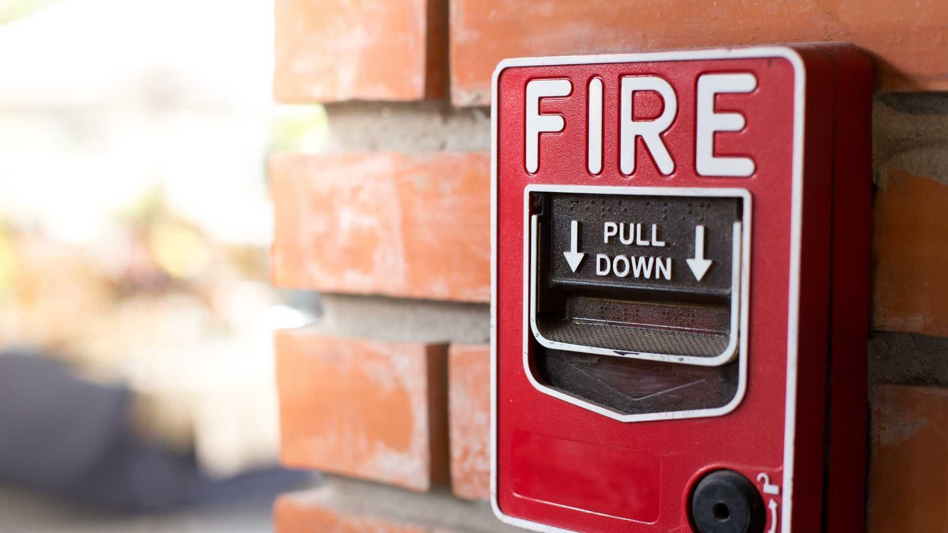 A red fire alarm is mounted on a brick wall.
