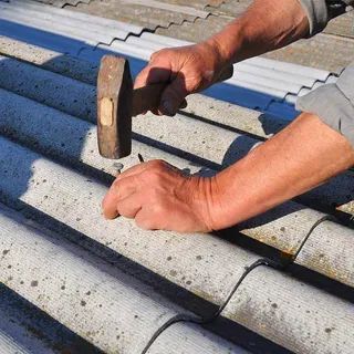 Hands hammering a nail into corrugated roofing tiles.