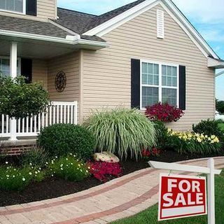 House for sale with tan siding, black shutters, and well-maintained landscaping.