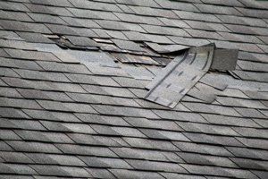 Damaged asphalt shingle roof, with missing and lifted shingles, showing wear and tear.