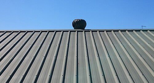 Metal roof with a spinning rooftop vent against a blue sky.