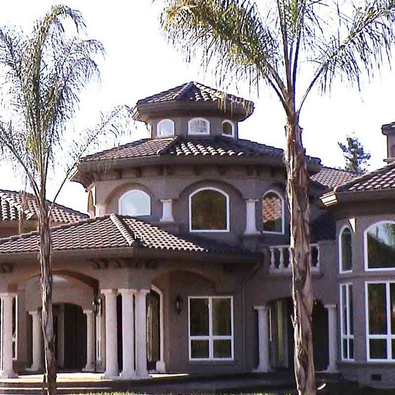 Two-story stucco home with a rounded turret and tiled roof, featuring arched windows and white columns.