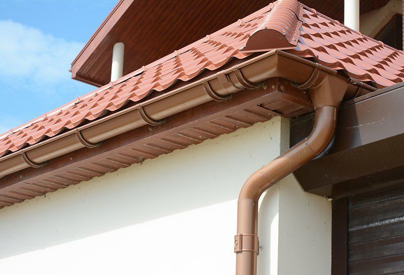 Brown gutters and downspout on a house with a brown tiled roof and white exterior wall.