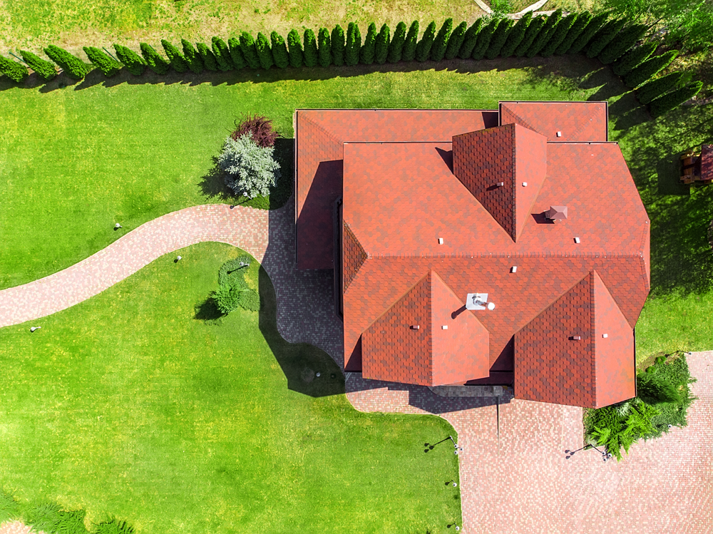 Overhead view of a house with a red roof, surrounded by green grass and a stone path.
