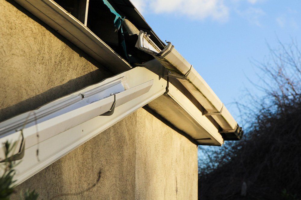 Close-up of a building's corner with gray gutters, a concrete wall, and a blue sky in the background.