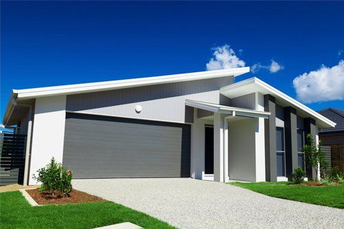 Modern house with gray garage door, gravel driveway, and a bright blue sky.