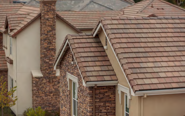 High-angle view of suburban houses with beige stucco walls, stone brick chimneys, and brown tiled roofs.