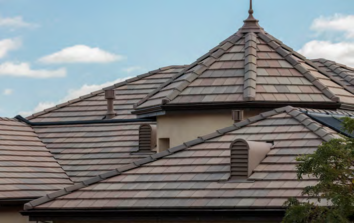 A residential roof with brown composite tiles, vents, a turret, and a clear blue sky background.