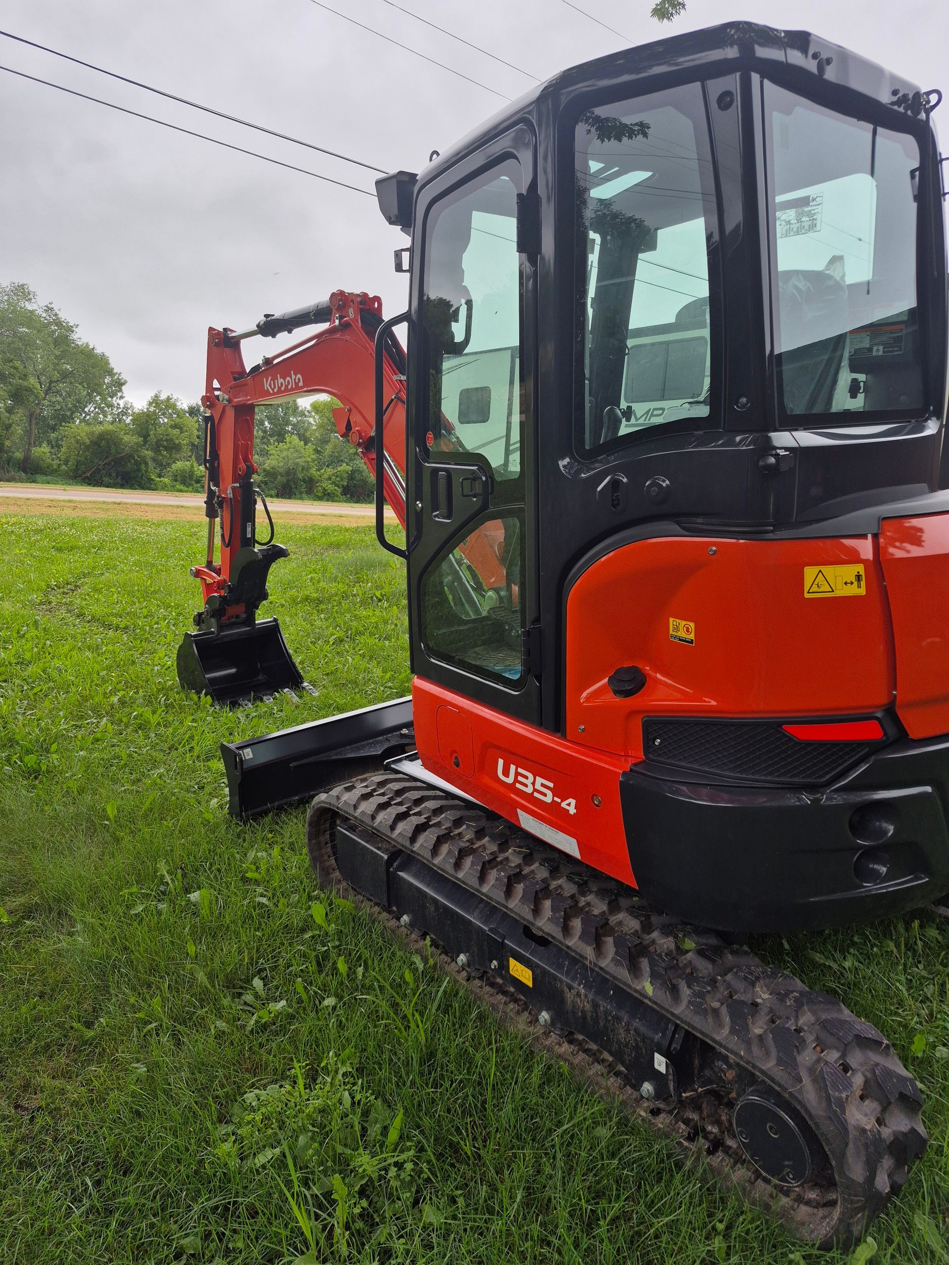 Orange Kubota excavator on green grass, parked outdoors, under cloudy sky.