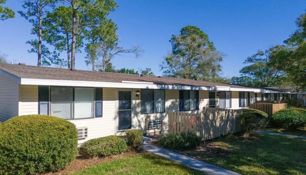 Apartment complex with beige siding, dark windows, and a brown roof under a blue sky.