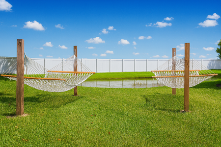 Two white hammocks suspended between wooden posts on a green lawn with a blue sky background.