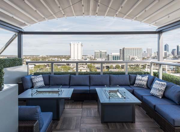 Rooftop patio with blue sectional seating, fire pit tables, and city views under a retractable canopy.
