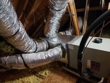 Insulated HVAC ducts and a white furnace unit in an attic with exposed wooden rafters