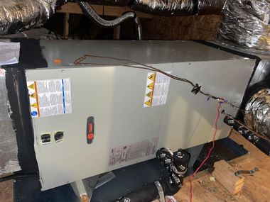 Furnace unit in attic with exposed ducts, wiring, and foil insulation around it.