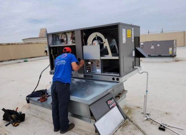 Technician servicing rooftop HVAC unit on a flat roof under an overcast sky