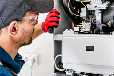 Technician in safety glasses and red gloves inspecting wiring inside an open machine panel