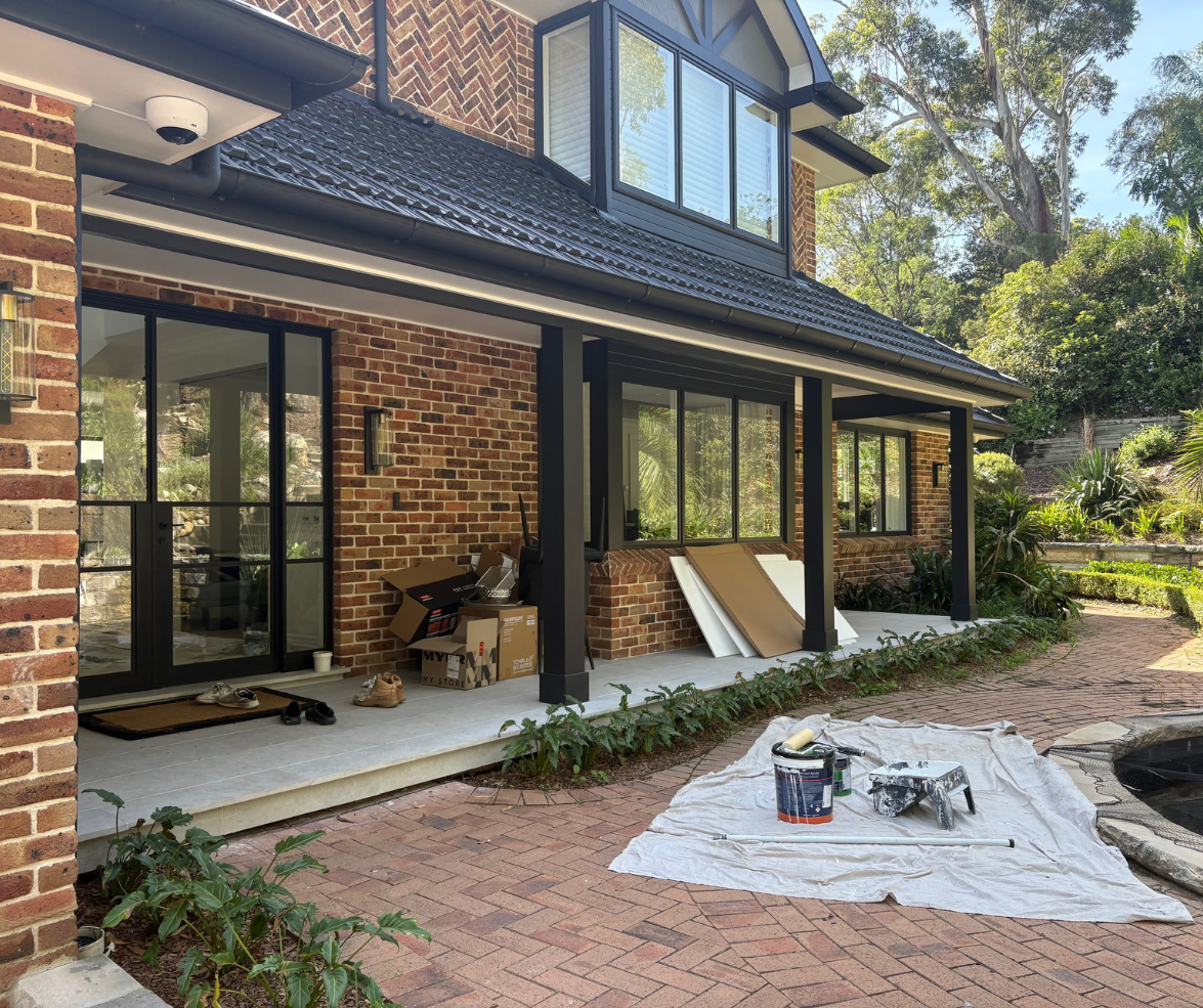 Brick house patio and backyard renovation with stacked boards, tools, and a covered walkway