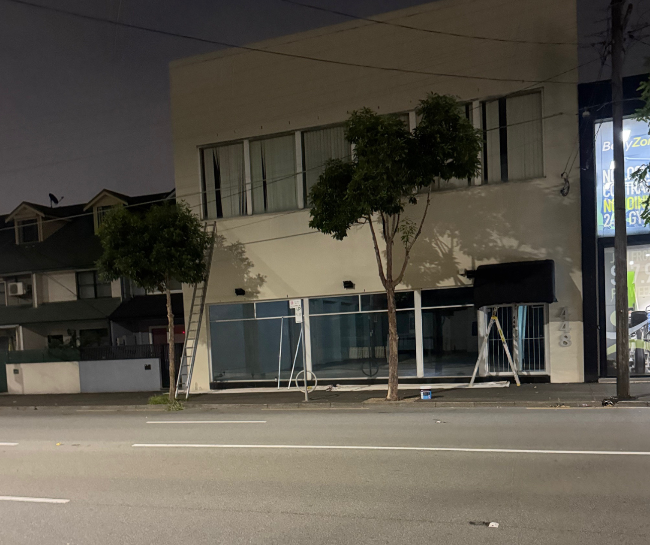 Empty storefront at night with trees, a sidewalk, and a quiet road in front